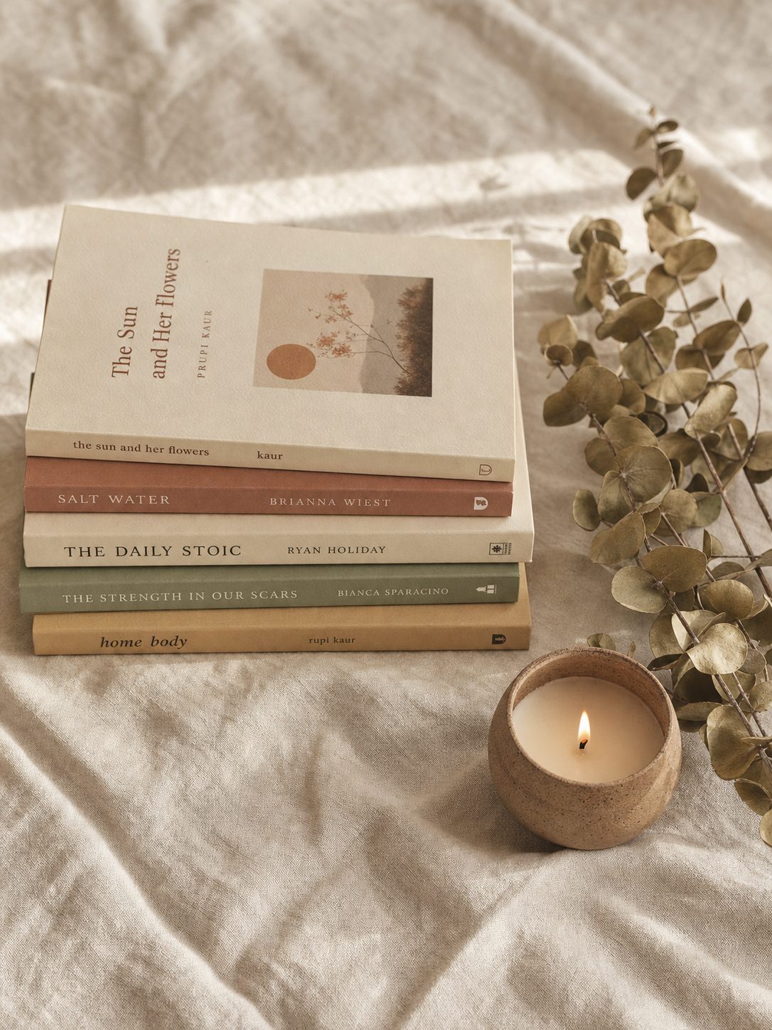 Stack of books with eucalyptus sprig and clay candle holder on cream linen